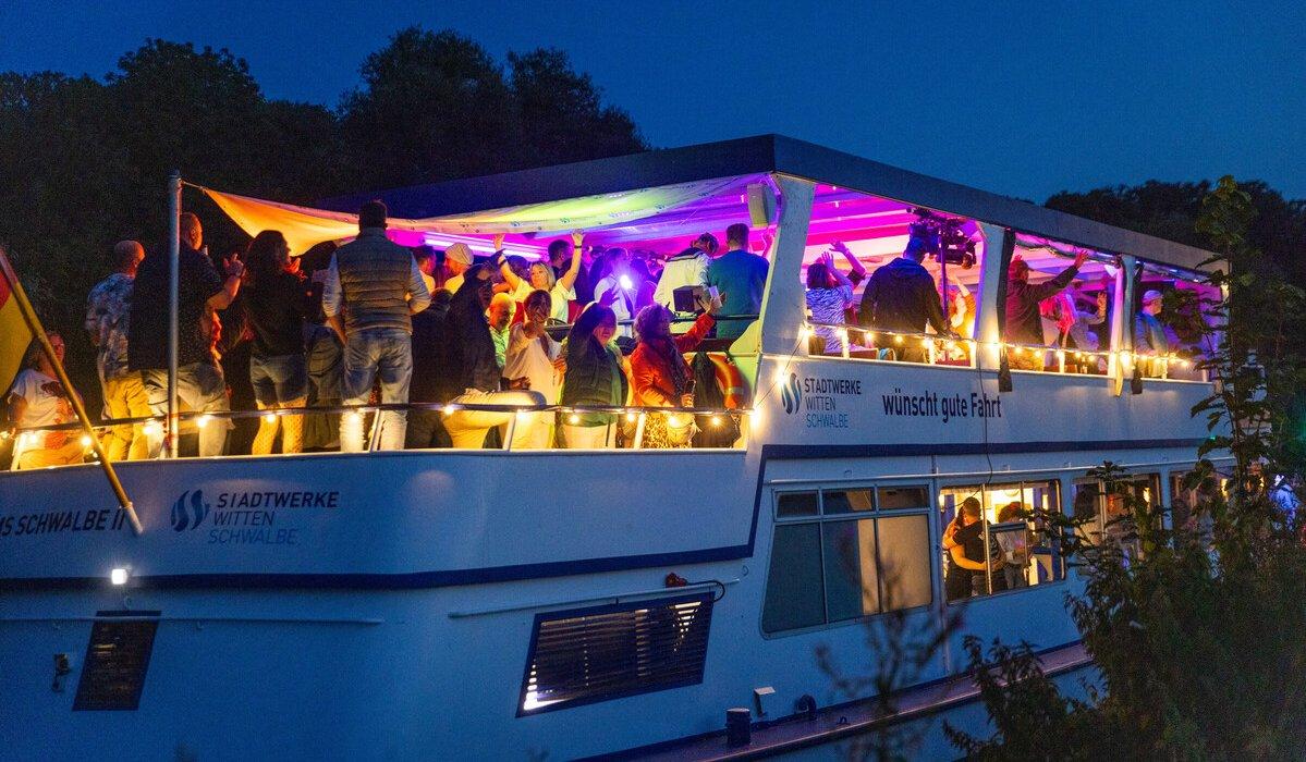 Personen bei Dunkelheit an Deck der beleuchteten Schwalbe